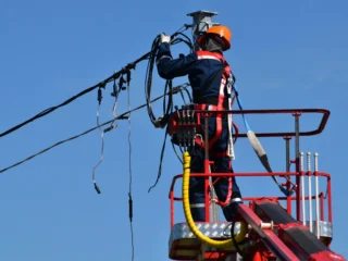 Technician performs maintenance on an overhead power line, highlighting the fragility of the energy system
