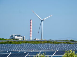 Solar farm and wind turbine next to industrial energy infrastructure under a clear sky.