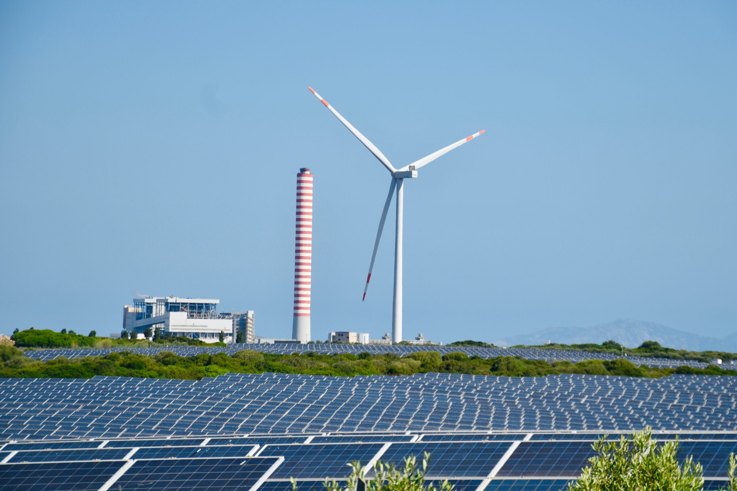 Solar farm and wind turbine next to industrial energy infrastructure under a clear sky.