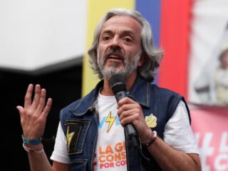 Juan Daniel Oviedo hablando en un evento de campaña en Colombia, vistiendo una camiseta con un rayo que representa energía y renovación política.