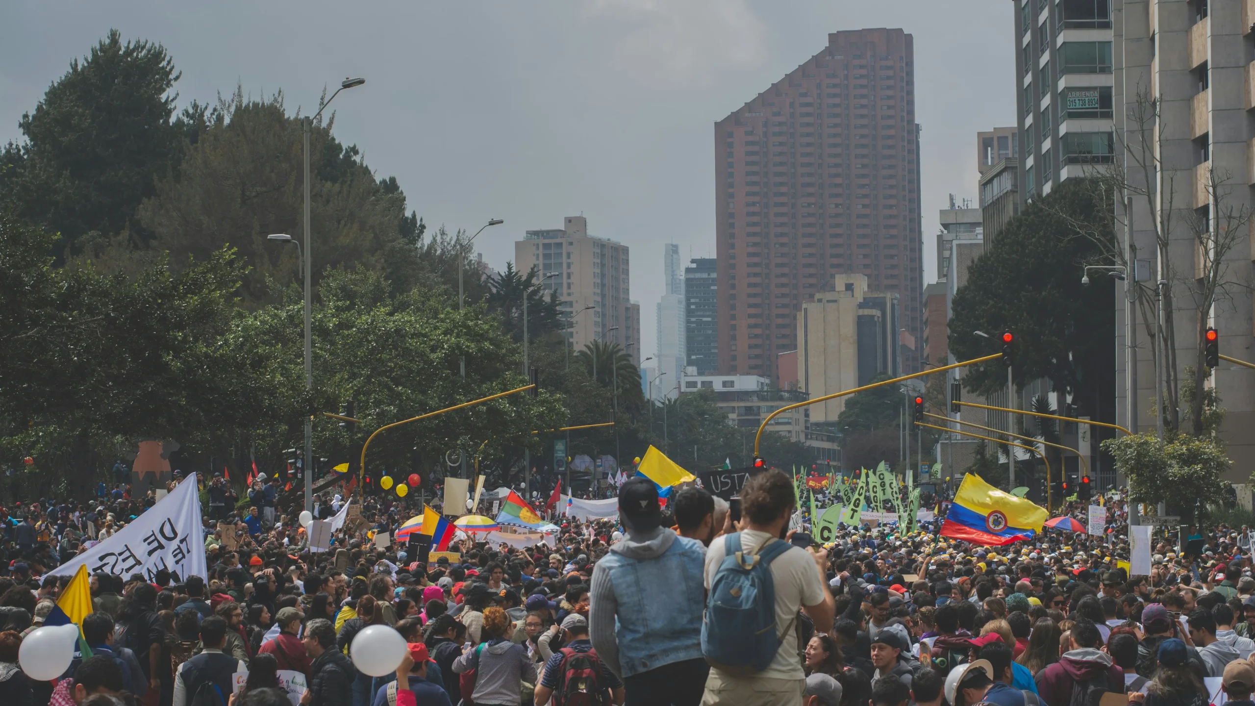 Crowd moving through a Bogotá avenue during a nighttime demonstration, surrounded by red traffic lights, urban buildings and dense city atmosphere, reflecting political tension and social uncertainty in Colombia ahead of the elections.