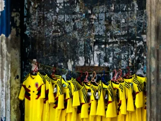 Camisetas de la Selección Colombia iluminan una fachada deteriorada en medio de un entorno urbano.