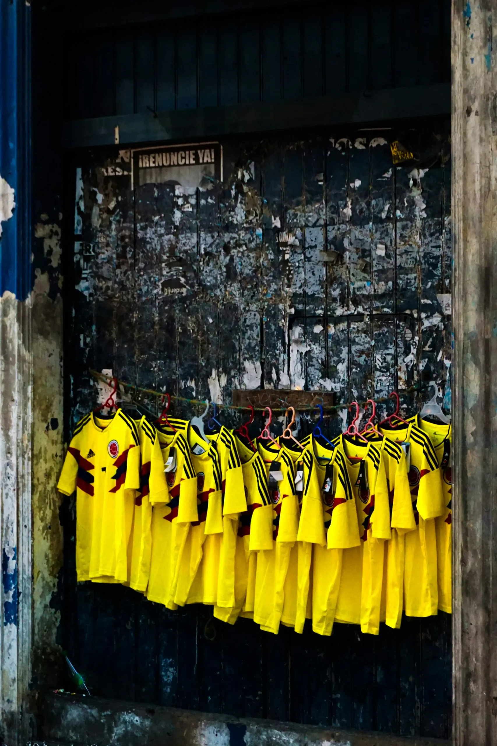 Camisetas de la Selección Colombia iluminan una fachada deteriorada en medio de un entorno urbano.